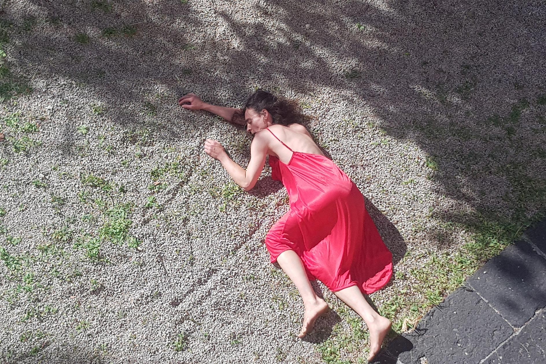 Eine Frau in einem roten Kleid liegt auf dem Boden der mit Kies bedeckt ist.